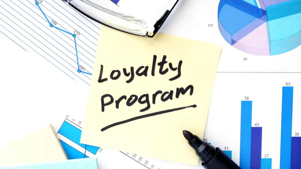 Sticky note labeled “Loyalty Program” placed over printed charts and graphs on a desk.